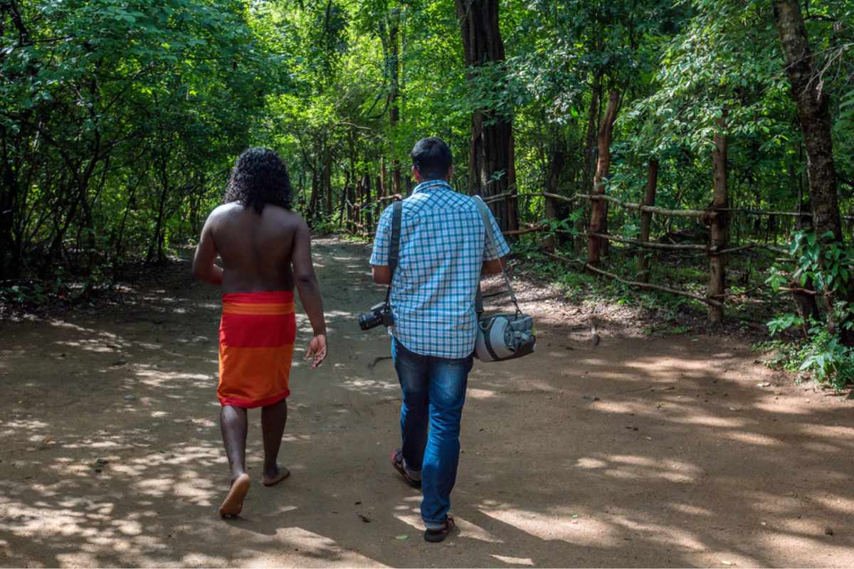 Vedda community member describes traditional attire to a traveller amidst the lush forests of Sri Lanka, symbolizing their deep connection with nature.