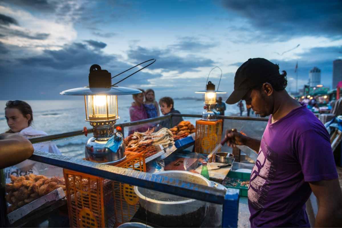 На площади Галле Фейс Грин в Шри-Ланке продавцы готовят и подают яркую уличную еду, демонстрируя оживленную кулинарную сцену этого места.